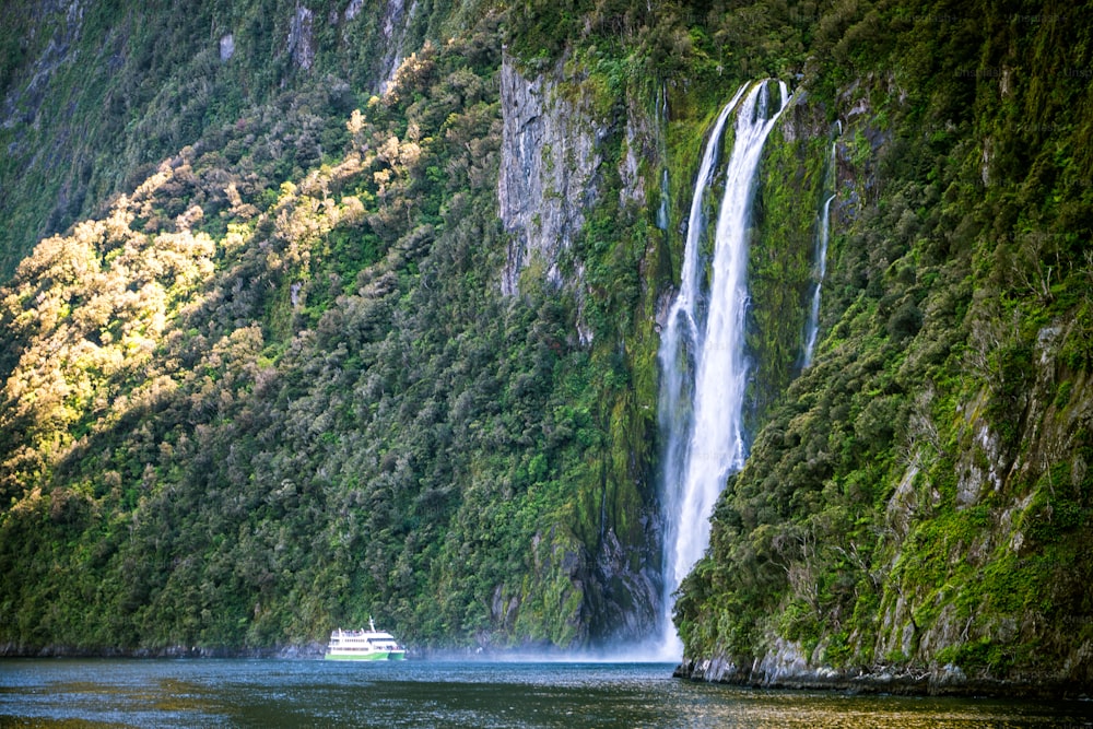 Barco de turismo que transporta pessoas turísticas se aproxima da grande cachoeira em Milford Sound. Belo cruzeiro panorâmico pelo Parque Nacional de Fiordland, na Ilha Sul da Nova Zelândia.