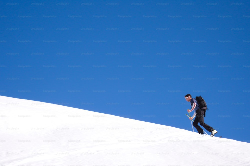 푸른 하늘 아래 아름다운 겨울날 자르간스 근처 스위스 알프스의 산봉우리로 가는 길에 가파른 눈 능선을 따라 하이킹하는 오지 스키 선수