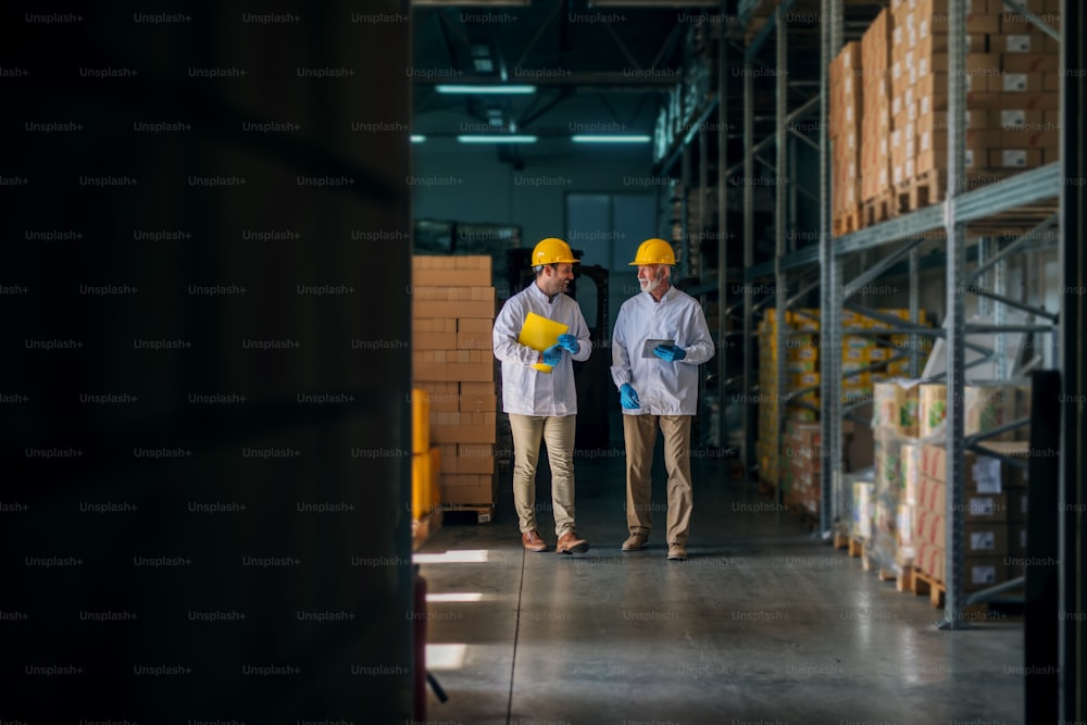 Cheerful father and son walking through their warehouse and talking about next steps in their business. Holding tablet and documents in their hands.