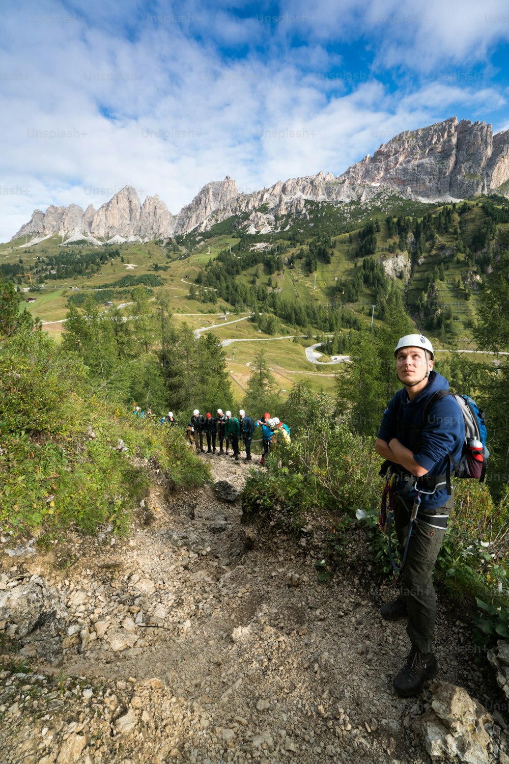 young male climber looks up at a Via Ferrata in the Dolomites in Alta Badia with great landscape and group of climbers behind him
