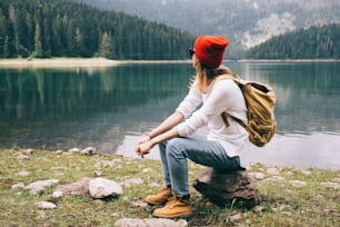 Muchacha excursionista solitaria que descansa junto a un lago de montaña.