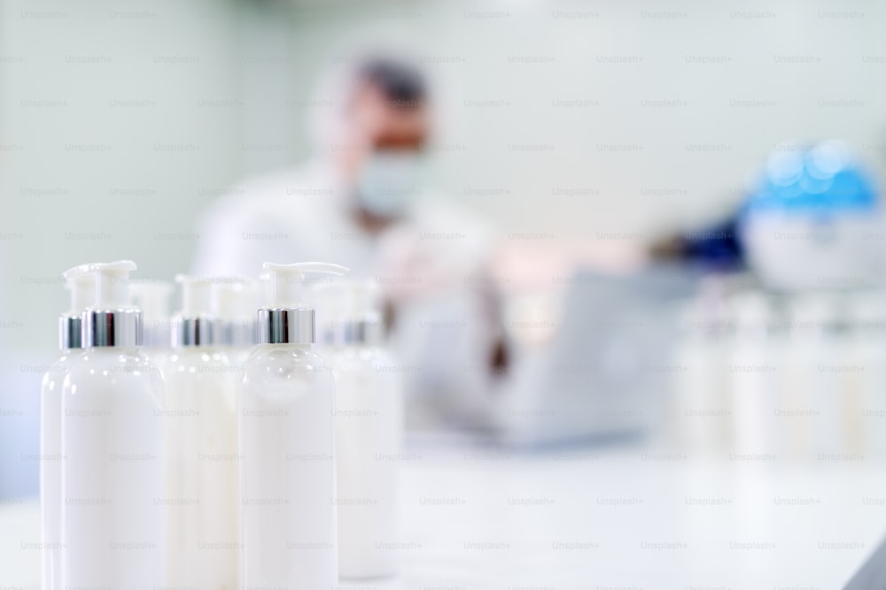 Close up of lotion bottles in bright laboratory. Blurred picture of man in sterile clothes in background.