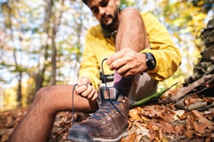 Close up do caminhante amarrando o sapato enquanto está sentado no chão na floresta no outono.