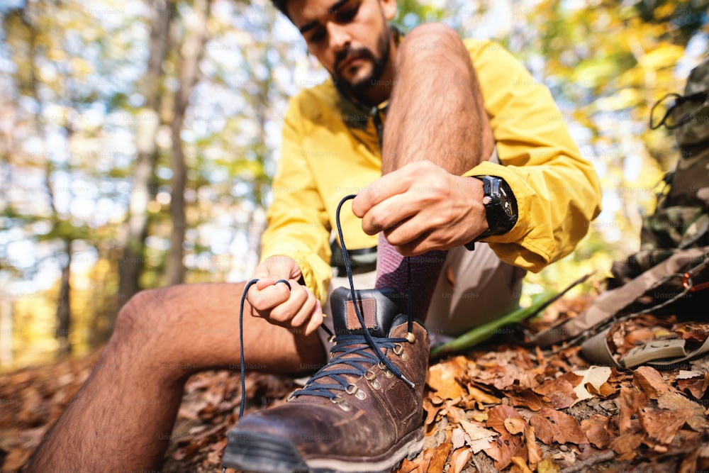 Close up of hiker tying shoe while sitting on the ground in the woods in autumn time.