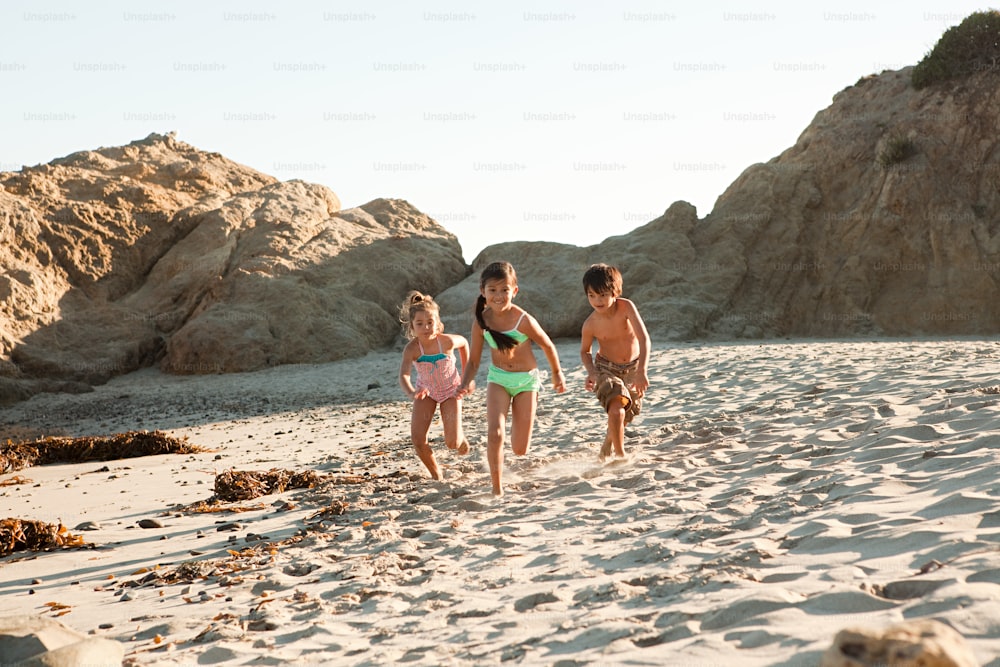 a group of young children running on a sandy beach