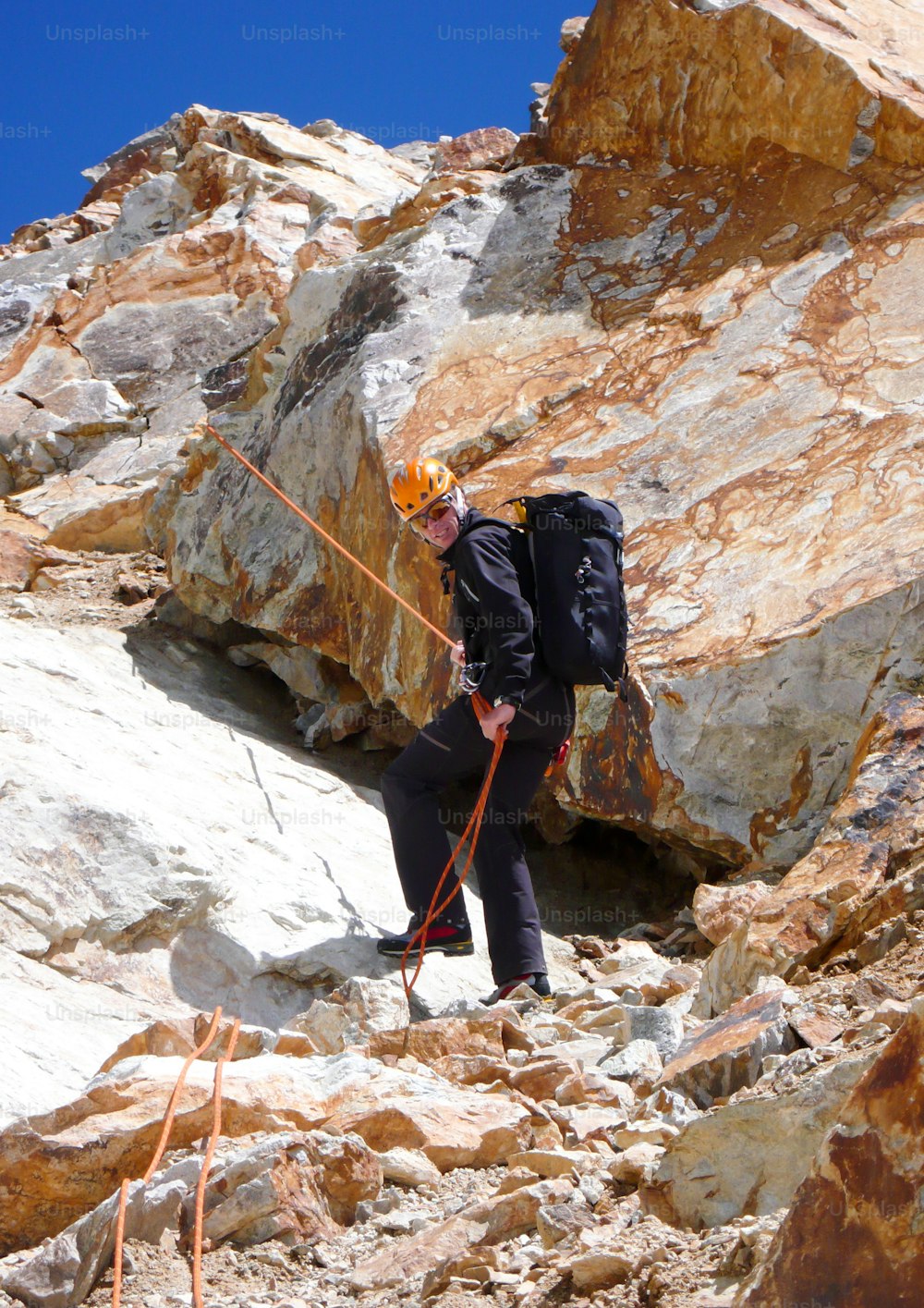 männlicher Bergführer Bergsteiger beim Abseilen über rote Felsen in den hohen Gipfeln und Bergen der Schweizer Alpen unter strahlend blauem Himmel bei Pontresina im Engadin