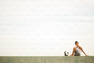 a woman sitting on a wall with a soccer ball