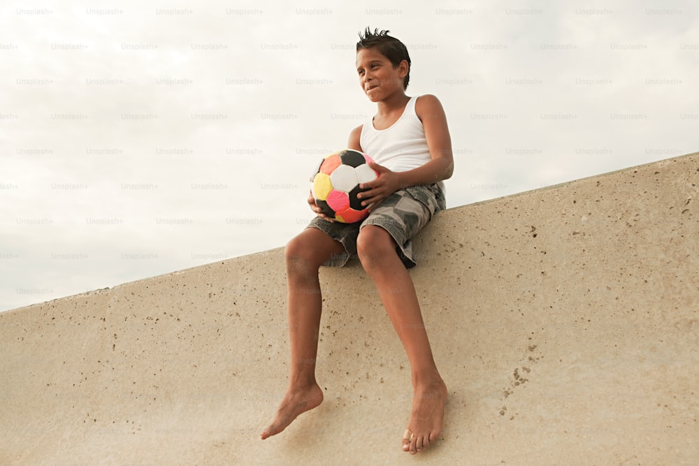 Ein Junge, der an einer Wand sitzt und einen Fußball hält