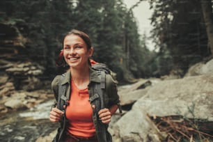 Cheerful attractive woman traveling near mountain river while spending weekend with pleasure