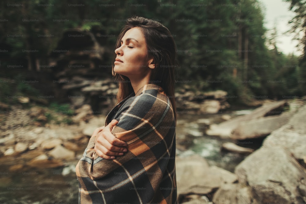 Pleasant thoughtful woman covering herself with a warm blanket and standing in the forest