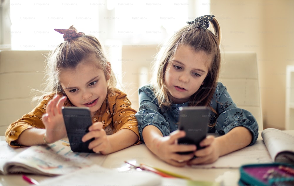 They each have their own tech toy. Two little school girls using smart phone.