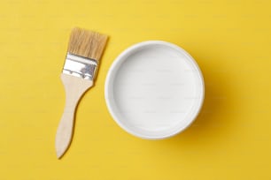 Pinceau et pot de peinture avec la couleur blanche sur fond jaune, vue de dessus