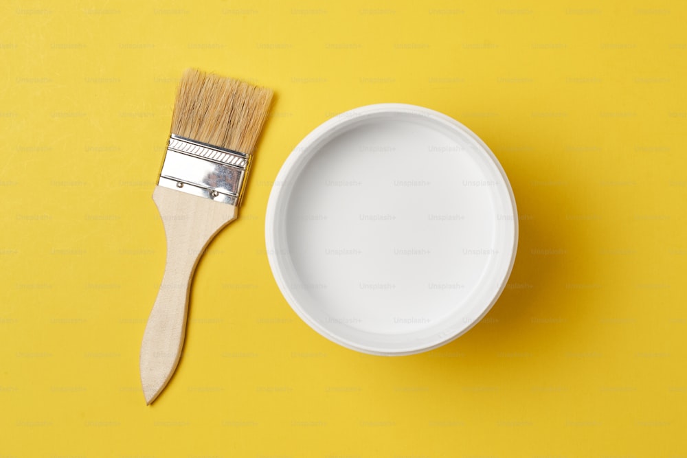 Brush and paint can with white color on yellow background, top view