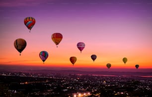 カラフルな熱気球は、光のカラフルと美しい夕暮れと日没の空の背景で来る暗くなる前に、日没時に街の上空を飛んでいます。