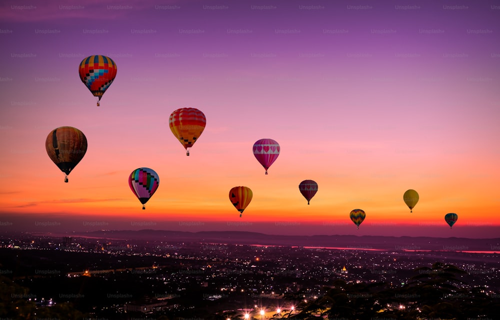 Die bunten Heißluftballons, die bei Sonnenuntergang vor Einbruch der Dunkelheit über der Stadt fliegen, kommen mit buntem Licht und einem schönen Dämmerungs- und Sonnenuntergangshimmelhintergrund.