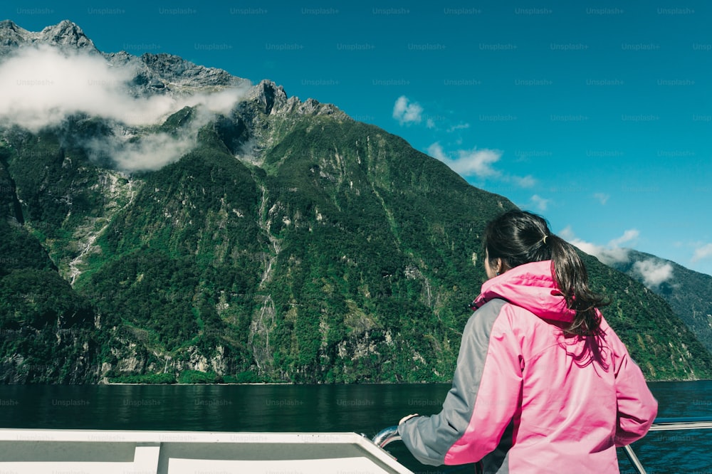 Giovane turista guarda lo scenario del fiordo dal ponte della nave a Milford Sound nel parco nazionale di Fiordland, nell'isola del sud della Nuova Zelanda. La crociera in barca a Milford Sound è l'attività principale per la maggior parte dei turisti.