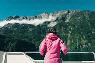 Una joven turista mira el paisaje del fiordo desde la cubierta del barco en Milford Sound en el Parque Nacional Fiordland, Isla Sur de Nueva Zelanda. El crucero en barco en Milford Sound es la actividad principal para la mayoría de los turistas.