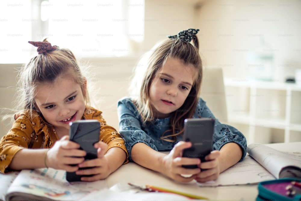 Each has its own phone. Two little school girls using smart phone.