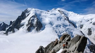 guide de montagne et un client masculin sur une crête rocheuse et enneigée se dirigeant vers un haut sommet dans les Alpes françaises près de Chamonix