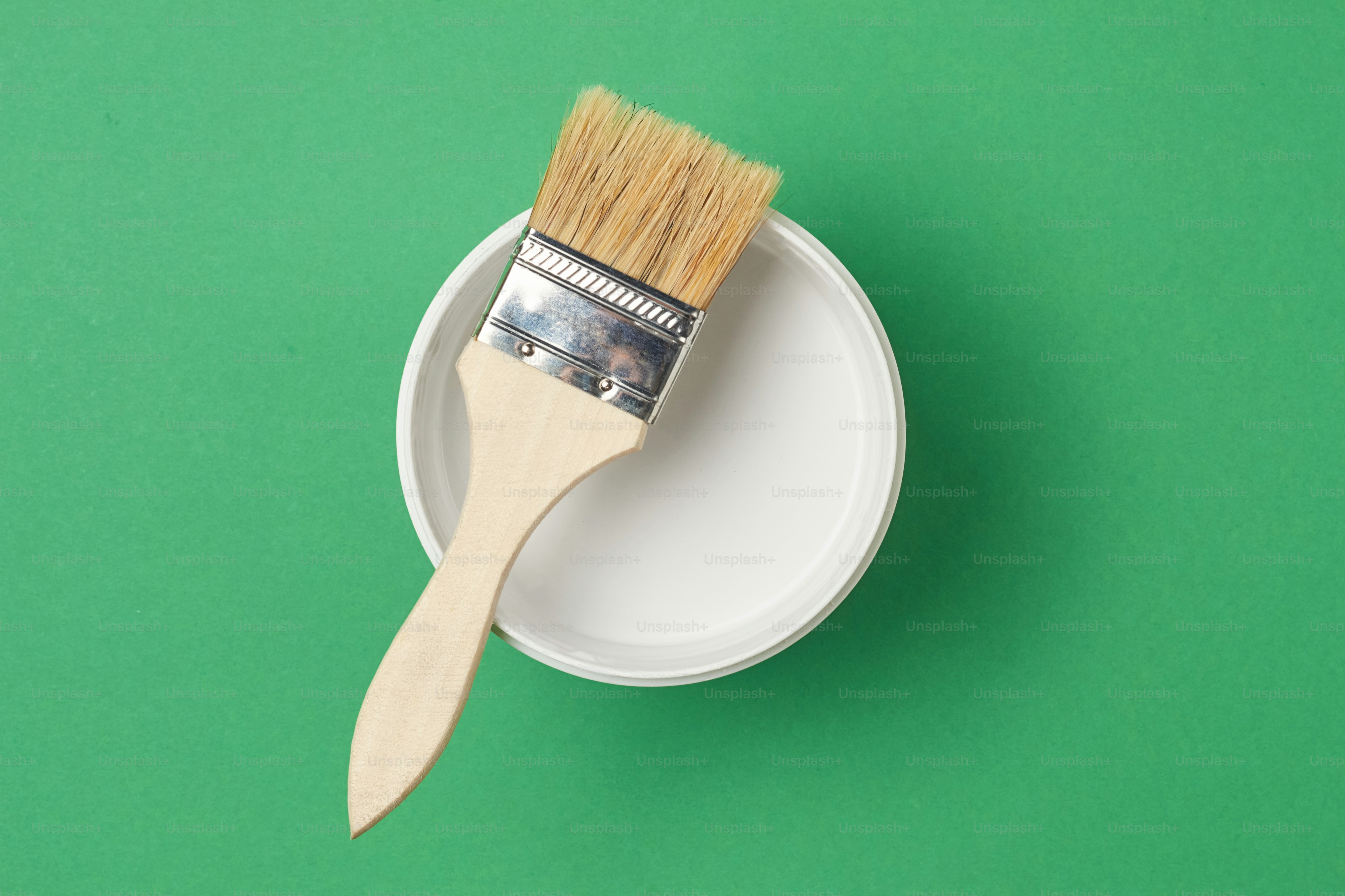 Brush and paint can with white color on green background, top view