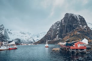 ノルウェーのロフォーテン諸島にある船漁船のあるハムノイ漁村で、赤いロルブの家があります。雪が降る中