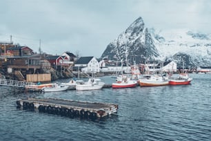 Jetée avec des bateaux dans le village de pêcheurs de Hamnoy sur les îles Lofoten, en Norvège, avec des maisons rorbu rouges en hiver