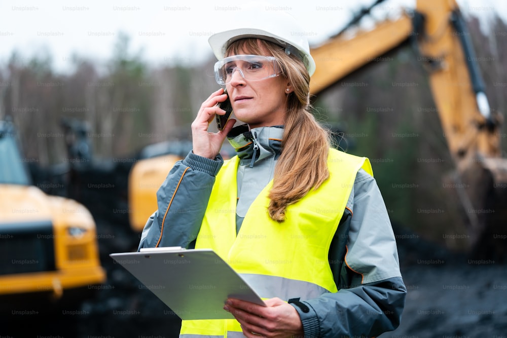 Mulher trabalhadora em mineração a céu aberto usando o telefone falando com o gerente