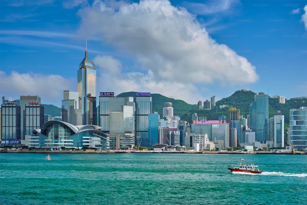 HONG KONG, CHINA - 1 DE MAYO DE 2018: Barco en el puerto de Victoria y el horizonte de Hong Kong en el paisaje urbano de los rascacielos del centro de la ciudad durante el día con nubes. Hong Kong, China.