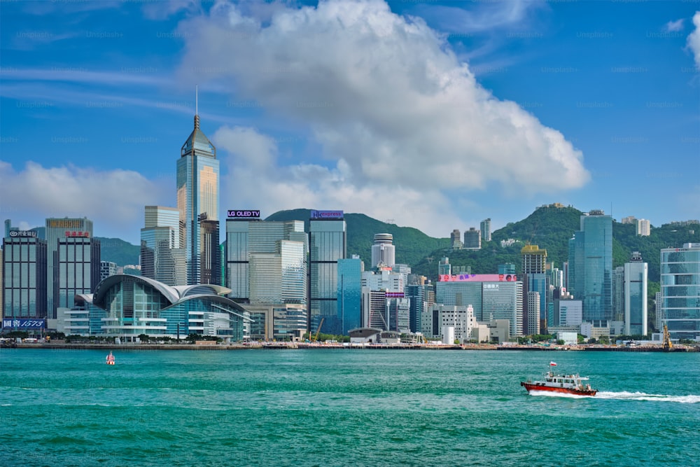 HONG KONG, CHINA - 1 DE MAYO DE 2018: Barco en el puerto de Victoria y el horizonte de Hong Kong en el paisaje urbano de los rascacielos del centro de la ciudad durante el día con nubes. Hong Kong, China.