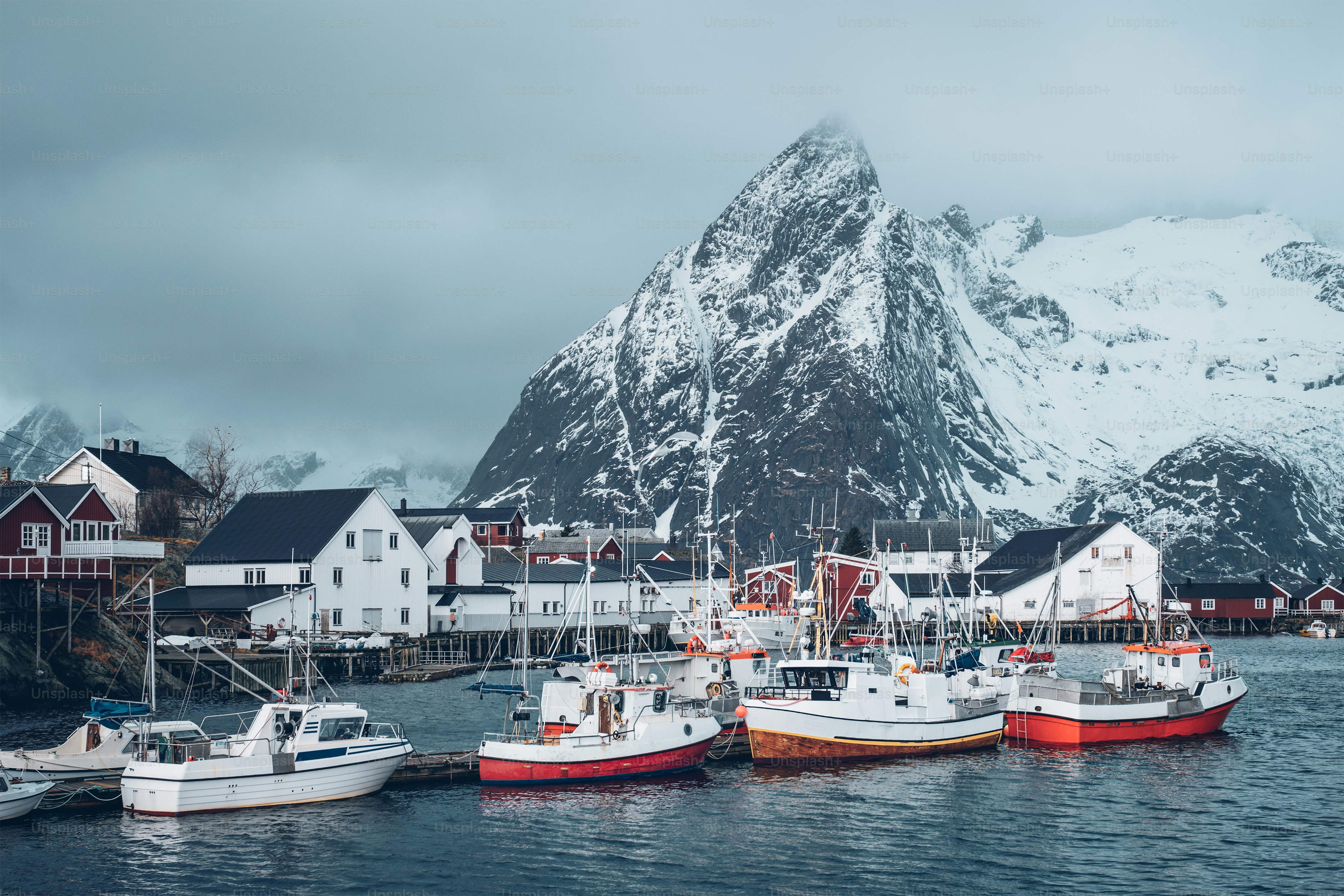 Pier mit Schiffen im Fischerdorf Hamnoy auf den Lofoten, Norwegen mit roten Rorbuhäusern im Winter