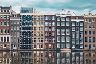 Fila di case tipiche e barca sul canale Damrak di Amsterdam con riflessione. Amsterdam, Paesi Bassi