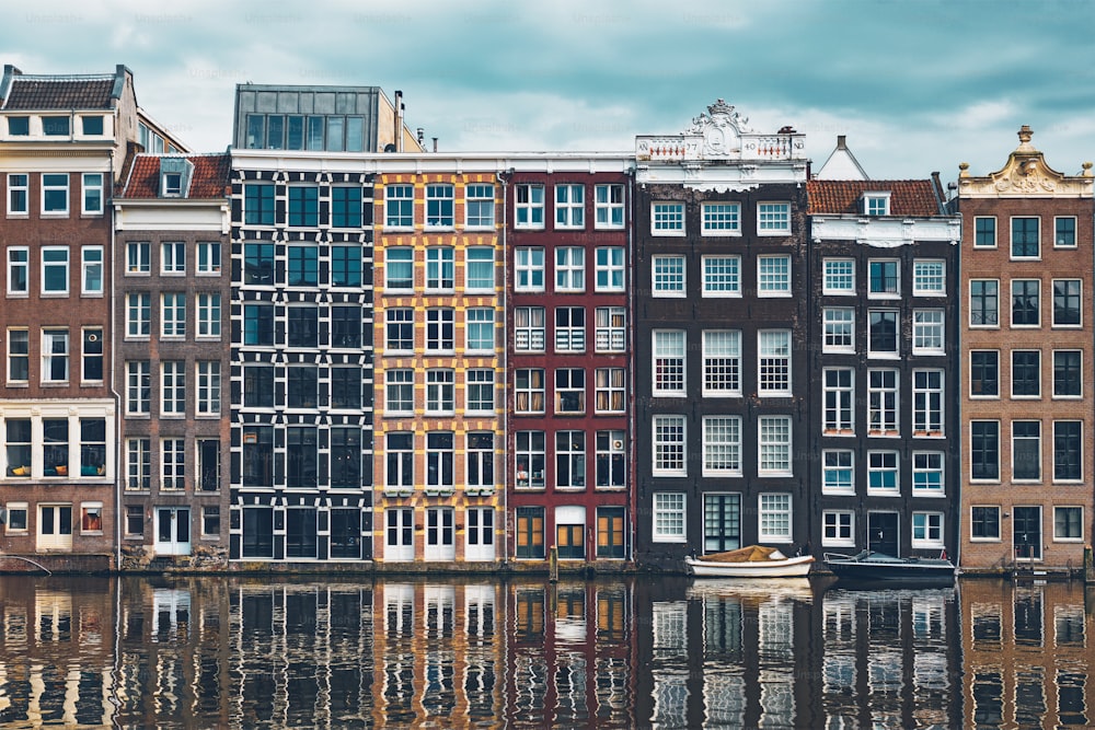 Hilera de casas típicas y barco en el canal Damrak de Ámsterdam con reflexión. Ámsterdam, Países Bajos