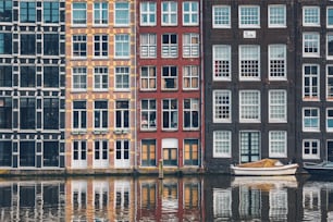 Row of typical houses and boat on Amsterdam canal Damrak with reflection. Amsterdam, Netherlands