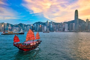 Hong Kong Skyline Stadtbild Innenstadt Wolkenkratzer über Victoria Harbour am Abend mit Junk Touristenfähre bei Sonnenuntergang mit dramatischem Himmel. Hongkong, China