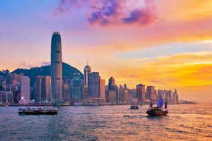 Hong Kong skyline cityscape downtown skyscrapers over Victoria Harbour in the evening with ferry boat and junk boat on sunset. Hong Kong, China