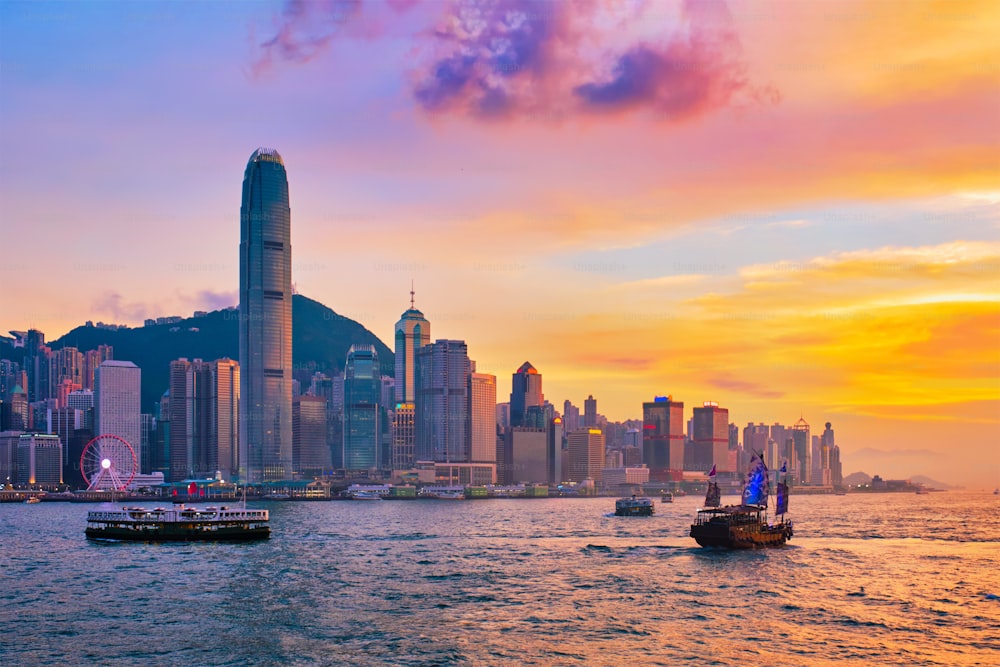 香港のスカイライン、街並み、ダウンタウンの高層ビル、夕方にはビクトリアハーバー、夕暮れ時にはフェリーボートとジャンクボート。香港、中国