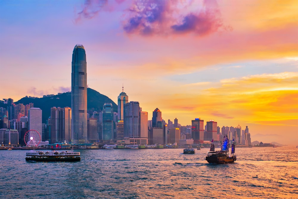 Gratte-ciel du centre-ville de Hong Kong au-dessus du port de Victoria le soir avec ferry et jonque au coucher du soleil. Hong Kong, Chine