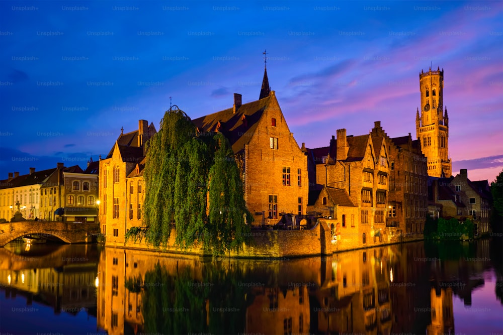 Vista famosa da atração turística de Bruges - Canal Rozenhoedkaai com campanário e casas antigas ao longo do canal com árvore na noite. Brugge, Bélgica