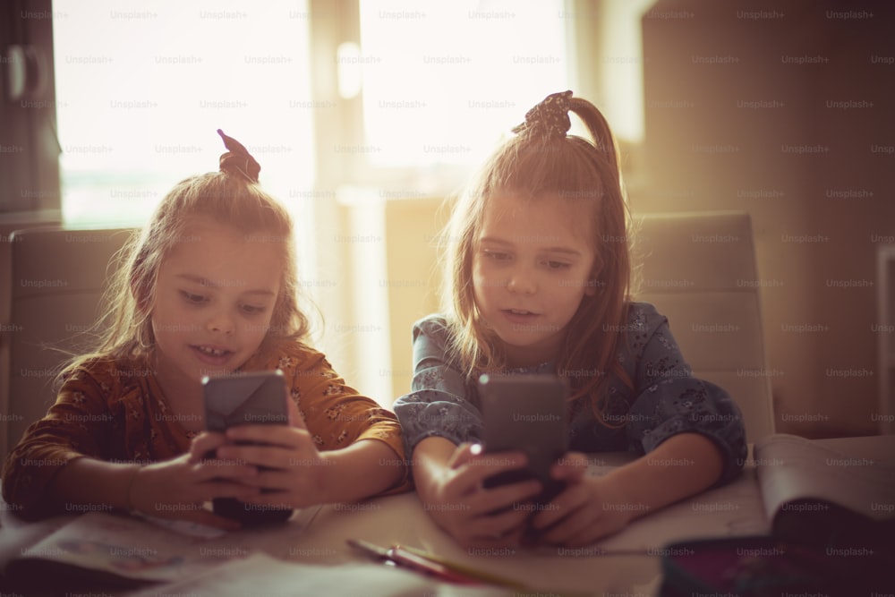 Each has its own phone. Two little school girls using smart phone.