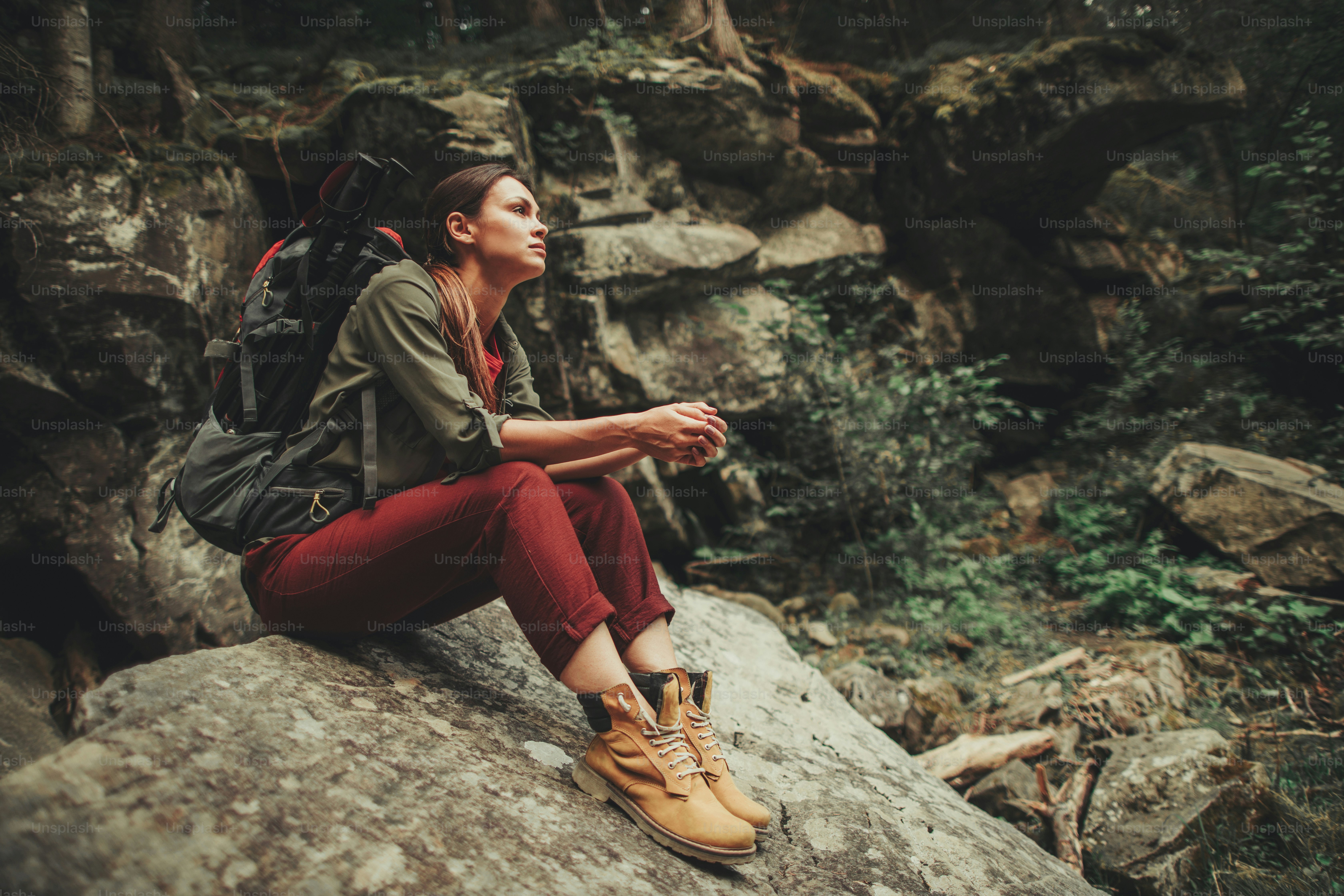 Thoughtful young woman spending an active weekend in the forest while sitting on the stone