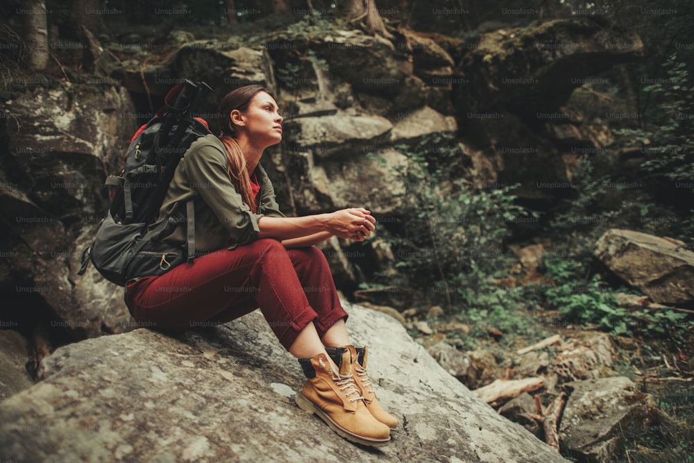 Jeune femme réfléchie passant un week-end actif dans la forêt assise sur la pierre