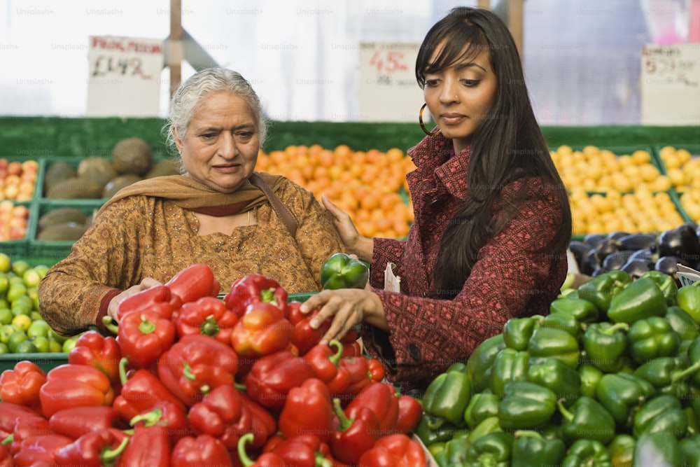 a couple of women standing next to each other in front of a pile of vegetables