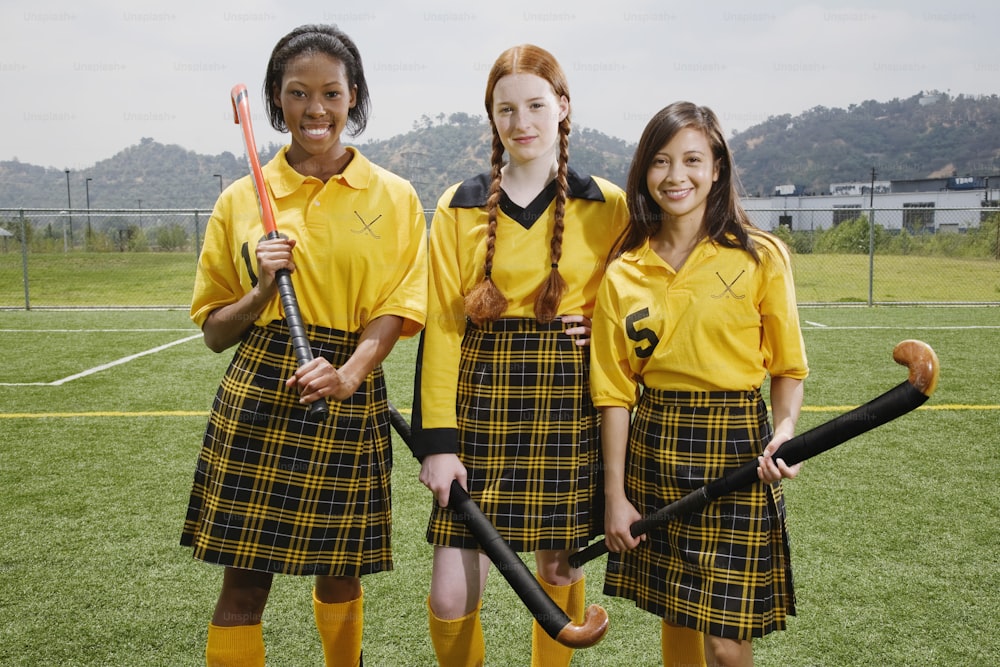 um grupo de três meninas em pé um ao lado do outro em um campo