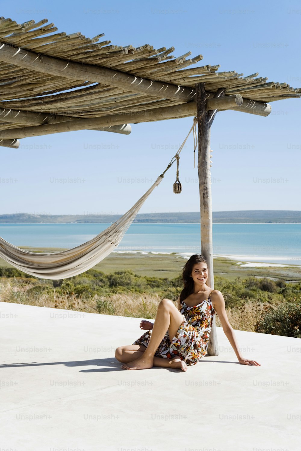 a woman sitting under a hammock next to the ocean