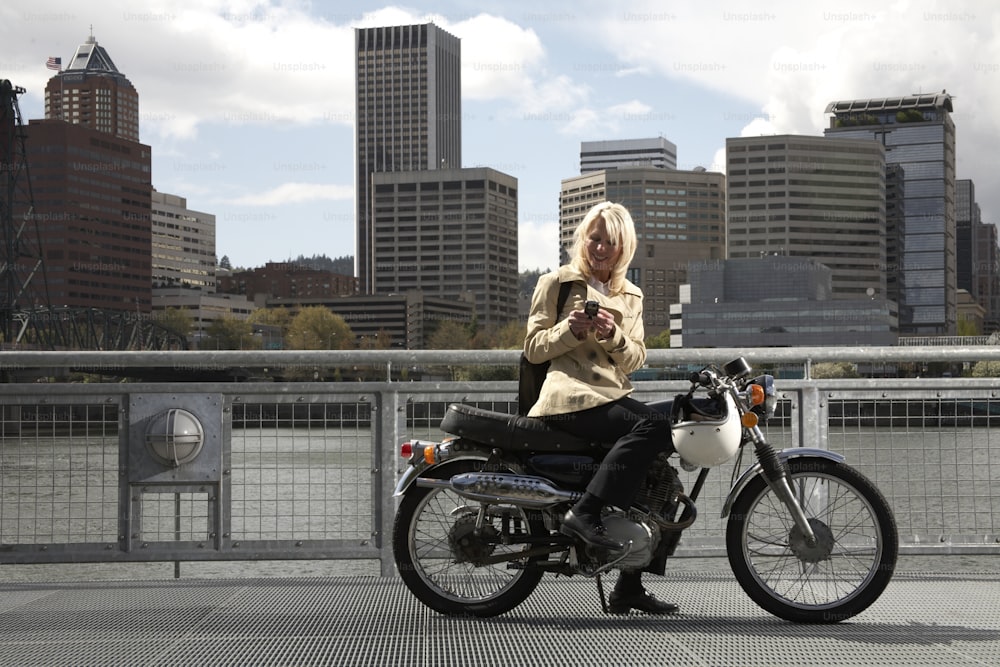 a woman sitting on a motorcycle looking at her cell phone