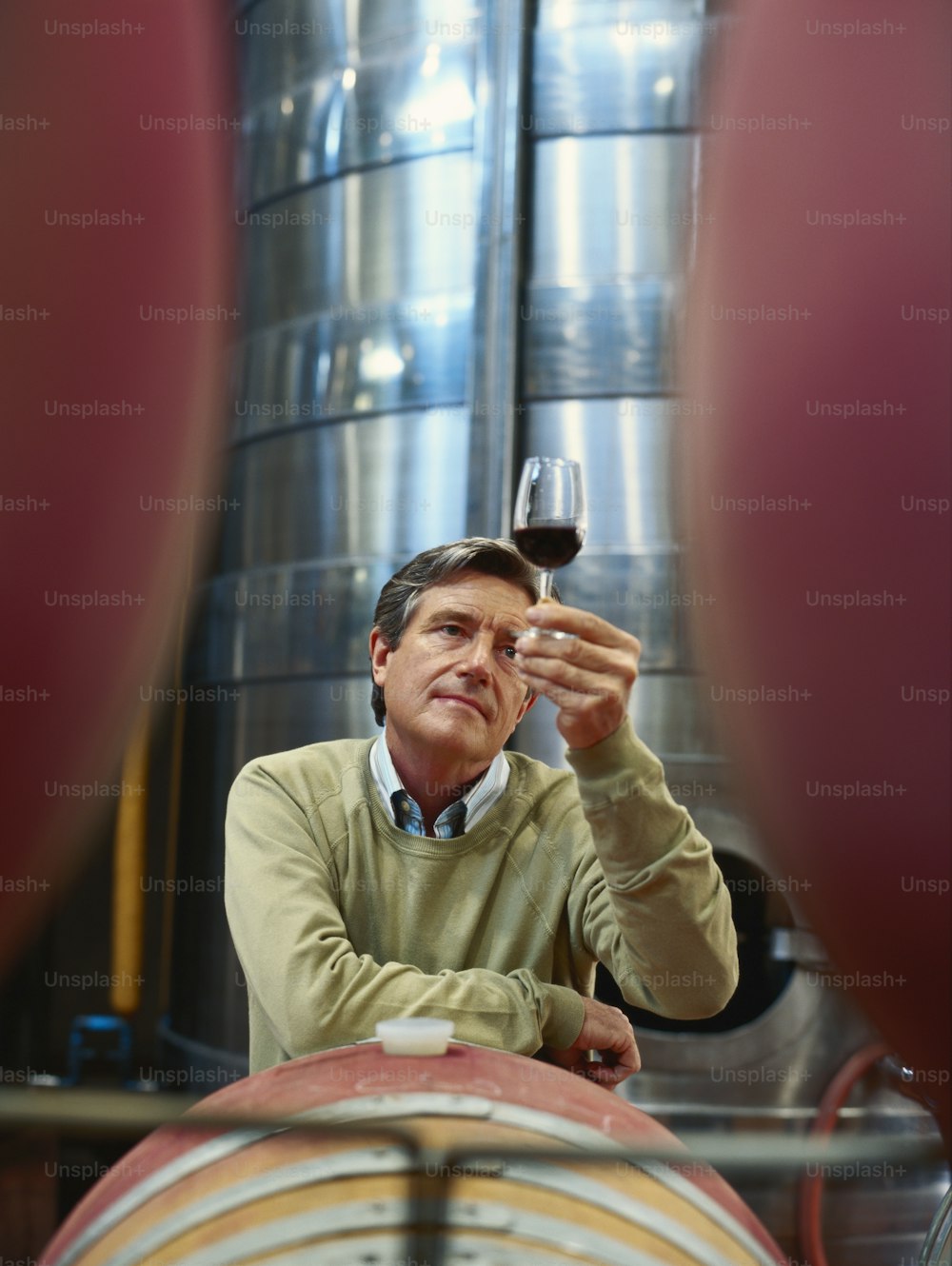 a man holding a glass of wine in front of a barrel