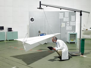 Un hombre arrodillado junto a un avión de papel