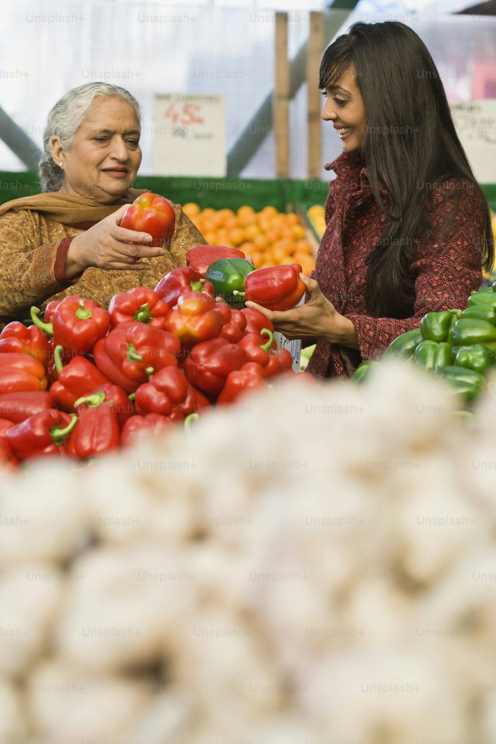 a couple of women standing next to each other near a pile of vegetables