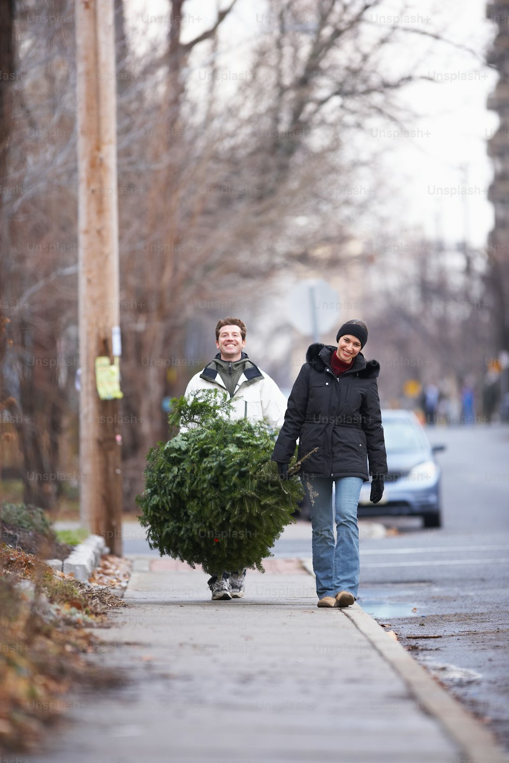 a man and woman walking down a sidewalk carrying a christmas tree