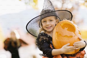 a little girl in a witch costume holding a pumpkin